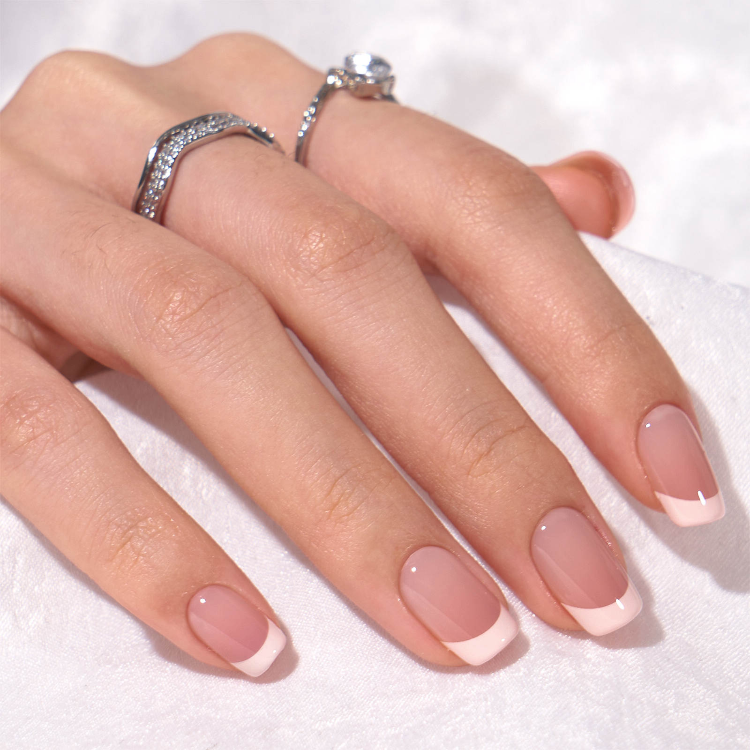 Hand model wearing short white French tip stick on nails with natural square shape