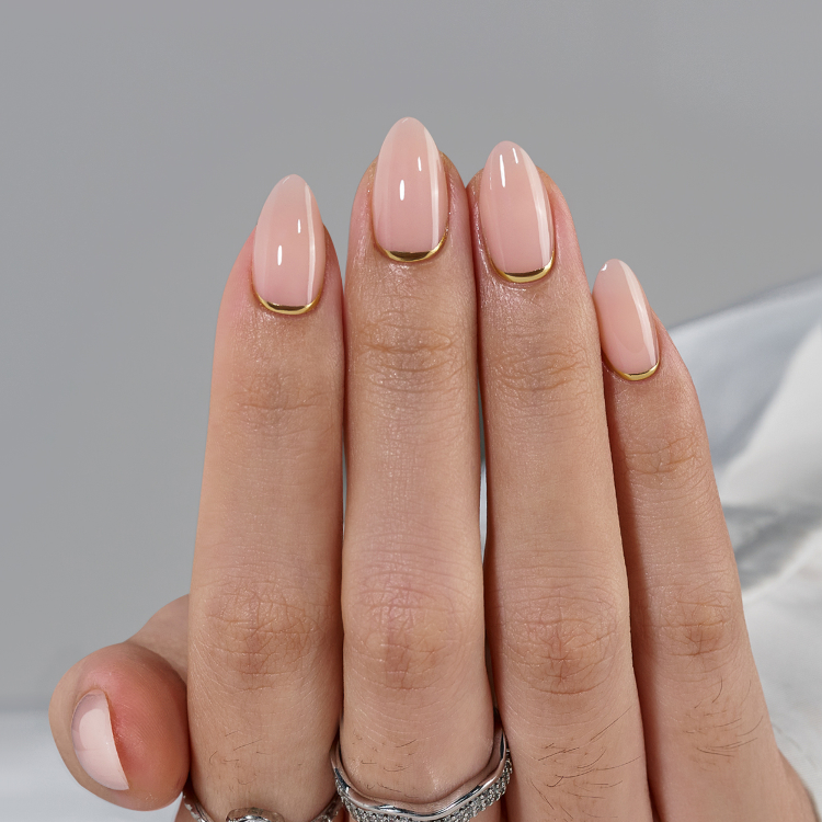 Hand model wearing nude gel press on nails in a natural almond style with gold accents